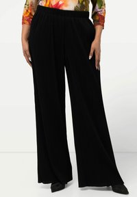 Pantaloni neri a gamba larga con un design a coste texturizzato; vita elasticizzata; abbinati a una blusa lunga a maniche con motivo floreale colorato e scarpe nere.