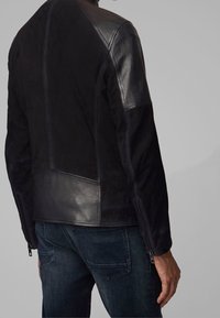 Svart läderjacka med en kombination av släta och mocka texturer, med dragkedjat ärmavslut och en skräddarsydd passform. Detaljerad sömnad genom hela jackan.