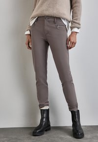 Slim-fit, gedempte grijze broek met een gladde textuur, voorzien van voorzakken met rits en een knopen sluiting, gecombineerd met zwarte enkellaarsjes.