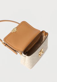 Kremowa torebka o teksturowanej powierzchni, z jasnobrązowym skórzanym wnętrzem, złotym zapięciem i łańcuszkiem, z subtelnym wzorem na zewnątrz.