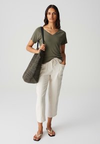 Olivgrünes V-Ausschnitt-T-Shirt, cremefarbene Jogginghose mit Kordelzug, schwarze Flip-Flops und eine dunkle Wäschettasche. Glatter Stoff und lockere Passform.