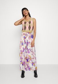 Bežs adīts bez piedurkņu tops ar rozā un brūnu argyle rakstu, kombinēts ar garu, plūstošu svārku ar ziedu apdruku purpura un dzeltenās krāsās.