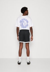 Witte graphic t-shirt met blauwe bedrukking met een klassiek ontwerp. Gecombineerd met zwarte mesh shorts, verfraaid met witte zijstrepen.