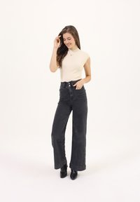 Jeans negros de tiro alto y pierna ancha con bolsillos frontales. Combinados con una blusa ajustada de color crema con trenzado y botas negras de tobillo.