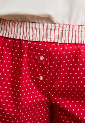 Pantaloncini pigiama rossi con pois bianchi e due bottoni, abbinati a una vita elastica bianca con strisce rosse.