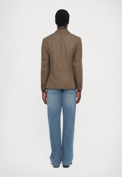 Brun rutig blazer med strukturerade axlar, parat med ljusblå vida jeans. Tydlig sömnad och subtila texturdetaljer.