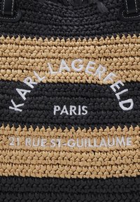 Czarna i beżowa tkanina w plecionkę z białym haftowanym napisem "Karl Lagerfeld Paris 21 Rue St-Guillaume."