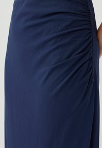 Kleid in Marineblau mit glatter Textur, das auf einer Seite Raffungen aufweist, die einen Drapierungseffekt erzeugen. Schlichtes, elegantes Design.