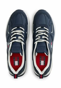Granatowe buty sportowe z materiału skórzanego, białe sznurowadła i czerwone wykończenie wewnętrzne. Posiada akcenty z logo oraz masywną białą podeszwę.