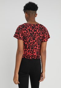 Top corto de manga corta rojo con un patrón de leopardo negro y un corte relajado. La parte de atrás cuenta con un escote redondo y mangas ligeramente abullonadas.