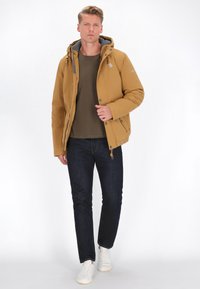 Geltonas pūkinis džemperis su pilka kapuce, priekinis užtrauktukas ir mygtukai; derinamas su tamsiomis džinsinėmis kelnėmis ir baltais sportbačiais, stovintis ant paprasto fono.