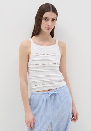 Weißes gestricktes Tanktop mit gerippter Textur, ausgestattet mit horizontalen Streifen und Lochmuster. Kombiniert mit hellblauen gestreiften Hosen.