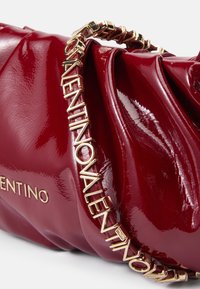 Červená kožená kabelka s lesklým povrchom, s textúrovaným dizajnom a zlatým reťazovým popruhom so nápisom "VALENTINO".