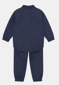 Mörkblå vadderad träningsoverall bestående av en jacka med ribbat krage och elastiska ärmslut, samt matchande byxor med elastisk midja.