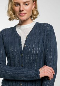 Marineblauer gestrickter Cardigan mit strukturiertem, geripptem Muster, gewelltem Kragen und sechs runden Knöpfen auf der Vorderseite.
