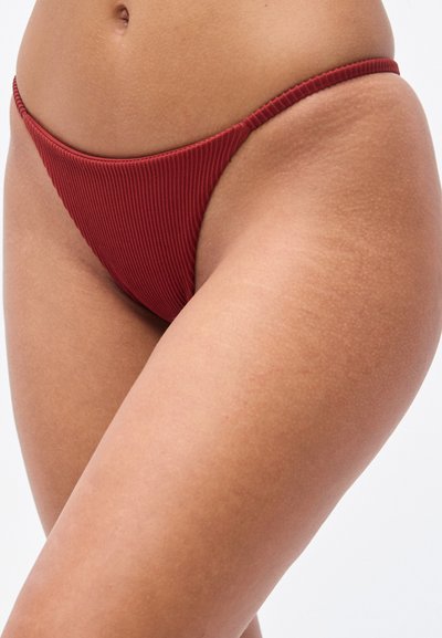 Κόκκινο σλιπ μπικίνι με ριγέ υφή, λεπτή μέση και λιτή κάλυψη. Η υφή είναι απαλή με έντονα ριγέ σχέδια.