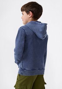 Sudadera azul de manga larga con textura suave, que cuenta con capucha y puños acanalados. Combinada con pantalones cortos de carga verdes oliva para un look casual.