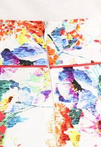 Sukně z látky s květinovým vzorem v živých barvách, se centrálním zipem a kontrastními červenými akcenty podél švů. Hladký povrch.