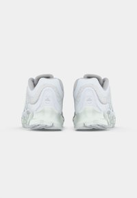 Hvite treningssko med teksturert overmateriale, grå detaljer og en tykk, gjennomsiktig såle. Har en rund form og polstret krage.