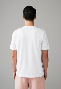Witte T-shirt met korte mouwen en een ronde hals. Glad katoen, ontspannen pasvorm, zichtbare stiksels, gedragen met lichtroze broek.