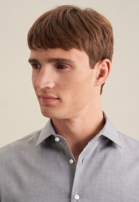 Camicia grigia chiara con colletto classico, caratterizzata da una morbida consistenza e un sottile motivo a trama, mostrata su uno sfondo neutro.