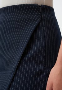 Gonna a righe navy realizzata in tessuto testurizzato, con cerniera laterale e sottili dettagli a pannello. Presenta delicate righe bianche per un effetto di contrasto.