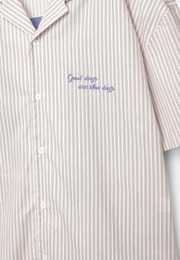 Camicia a righe di colore chiaro con linee viola. Presenta un colletto e testo ricamato: "I giorni belli sono giorni lenti."