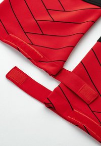 Roter Stoff mit einem geometrischen schwarzen Muster, ausgestattet mit verstellbaren Trägern mit Klettverschluss. Glatte Textur, schlankes Design.