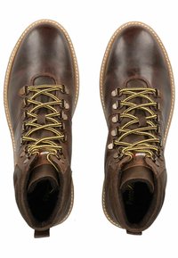 Hnědé kožené outdoorové boty s žlutými tkaničkami, kovovými háčky a texturovaným povrchem. Mají polstrovaný límec a kontrastní bílé švy.