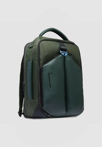 Zaino verde con una combinazione di tessuto strutturato e dettagli in pelle liscia, caratterizzato da un ampio scomparto con cerniera e una maniglia robusta.