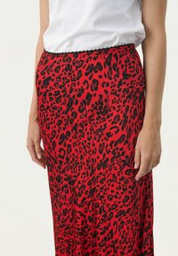 Red leopard print skirt with a black elastic waistband, made from a smooth fabric. Features a flowing design, knee-length cut, and a vibrant pattern.