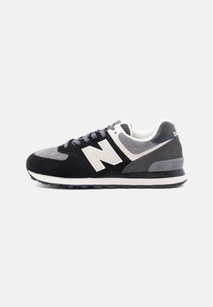 Baskets basses New Balance en noir, gris et blanc avec panneaux en daim et tissu, fermeture à lacets, et logo sur le côté et le talon.