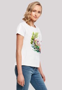 White cotton t-shirt features a vibrant floral design with green leaves and colorful flowers on the front. Short sleeves and relaxed fit.