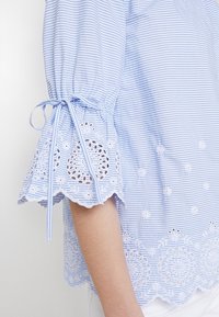 Light blue striped blouse with ruffled sleeves, featuring lace trimming and embroidered floral designs. Soft, lightweight fabric.