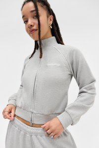 Svetlo šedá krátka bunda na zips s vysokým golierom, rebrovanými manžetami a lemom. Obsahuje biele švy, logo a mäkkú, textúrovanú tkaninu.