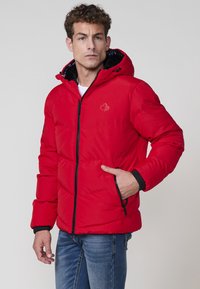 Chaqueta acolchada roja con cierre frontal de cremallera, puños elásticos y capucha. Incluye un logo bordado y bolsillos laterales con acentos en negro.