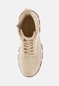Scarpa sportiva beige con tomaia testurizzata, punta rotonda, design con lacci e suola in gomma marrone. Presenta il logo sulla fodera interna e una cerniera.