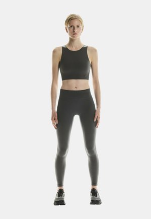 Un crop top de sport noir et un legging taille haute, tous deux en tissu lisse et extensible, associés à des sneakers sombres.