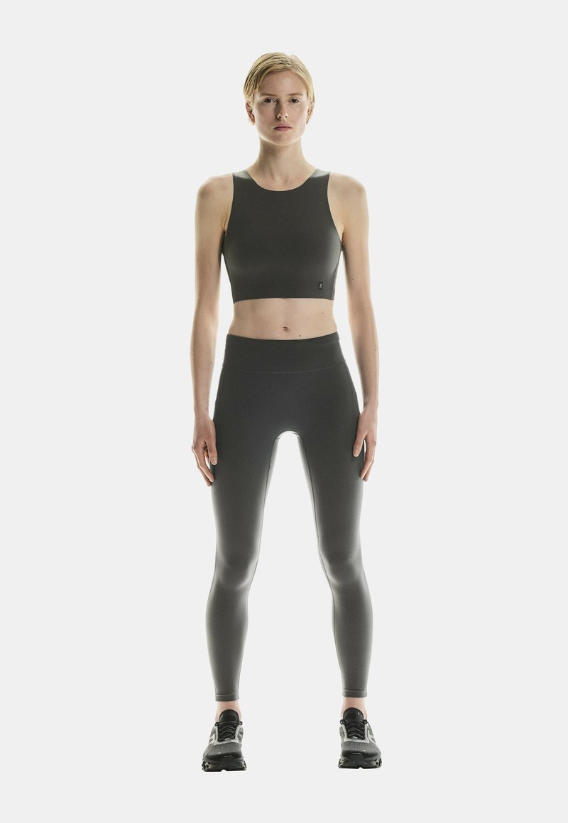 Must mustus musteede crop top ja kõrge vöökohaga retuusid, mõlemad valmistatud siledast, venivast kangast, kooskõlas tumedate spordijalatsitega.