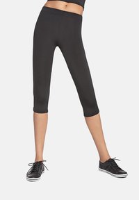 Czarne legginsy capri wykonane z elastycznego materiału, o gładkiej strukturze i elastycznym pasie. Połączone z czarnymi sneakersami na sznurowadła.