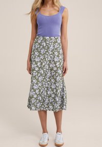 Violetti ribattu tank-top ja kukkakoristeinen oliivinvihreä midihame, jossa on valkoisia ja vaalean violetteja terälehtiä, yhdistettynä valkoisiin tennareihin.