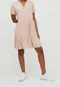 Short-sleeve, pink dress with a V-neck and tiered ruffle hem. Worn with white sneakers, fabric appears light and smooth.