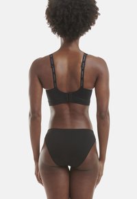 Černá sportovní podprsenka s nastavitelnými ramínky, na kterých je logo značky, v kombinaci s černými kalhotkami. Hladký povrch, jednoduchý design a plné pokrytí.