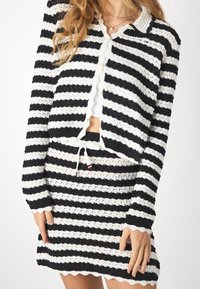 Svart och vit randig stickad cardigan och matchande kjolset med vågiga kanter och dragsko i midjan. Materialet är mjukt och strukturerat.