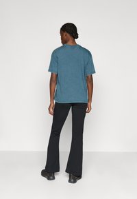 Teal színű pamut póló, laza szabással, rövid ujjal és kerek nyakkal, fekete trapéznadrággal és sötét cipővel párosítva.