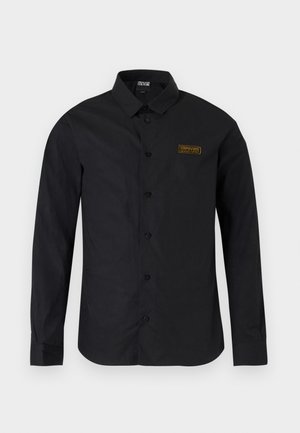 Camisa negra de manga larga con botones, cuello y una pequeña parche rectangular con el logotipo dorado en el pecho izquierdo.