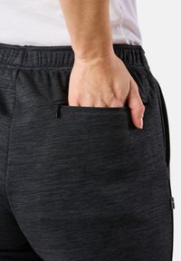 Grå atletiska byxor i strukturerad tyg, med en sidficka med dragkedja och en accentfärg detalj vid fållen.