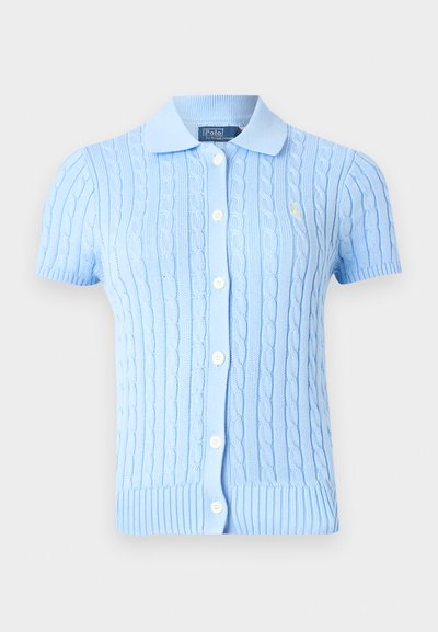 Gaiši zilā īss piedurkņu adītais kardigans ar baltām pogām un nelielu izšūtu logotipu uz krūtīm, ar šauru apkakli.