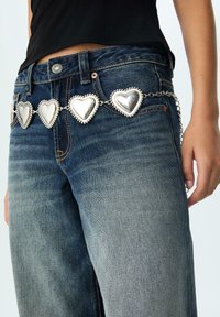 Dżinsy z średnim stanem mają srebrny pasek w kształcie serca, z każdą sercem podkreślonym koralikowym detalem, co doskonale współgra z niebieskim materiałem.