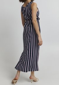 Laivansininen ilman hihoja oleva mekko, jossa on pystyharmaita vaaleanpunaisia raitoja, vyötärö on muotoiltu ja helman pituus ulottuu lattiaan. Silkkinen kangas, jossa on kevyt kiilto.